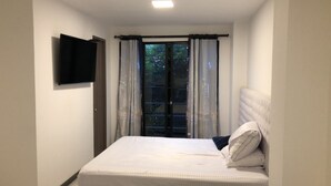 Un dormitorio con cama, televisor en la pared y ventana con cortinas.