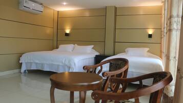 A hotel room with two beds, a wooden chair, a small table, and an air conditioning unit on the wall.