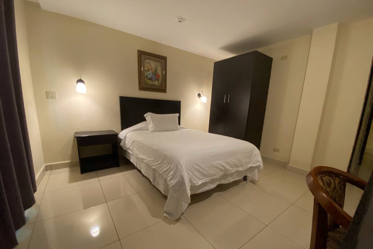 A bedroom with a bed, nightstands, a wardrobe, and a painting on the wall.