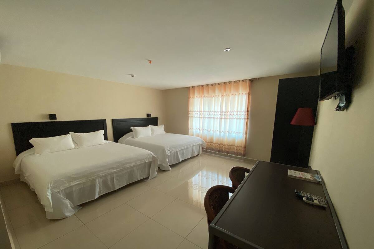 A hotel room with two beds, a desk, a chair, a TV, and a window with curtains.