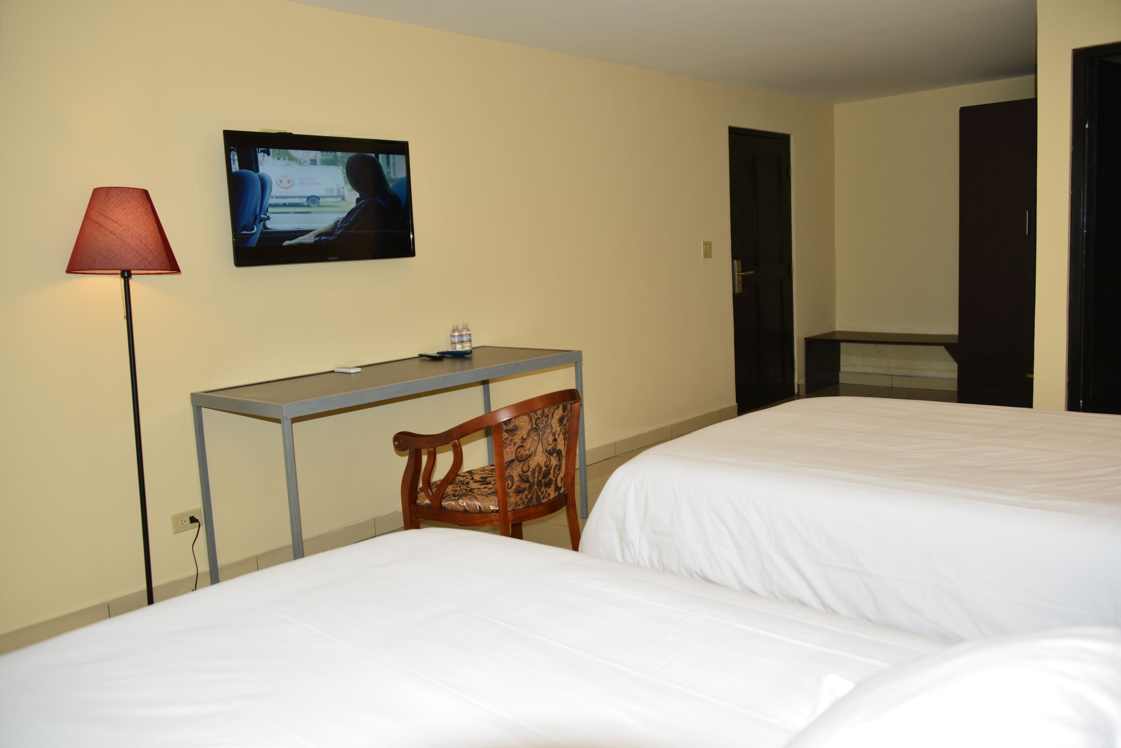 Habitación de hotel con dos camas, un escritorio, una silla, un televisor en la pared y una lámpara.