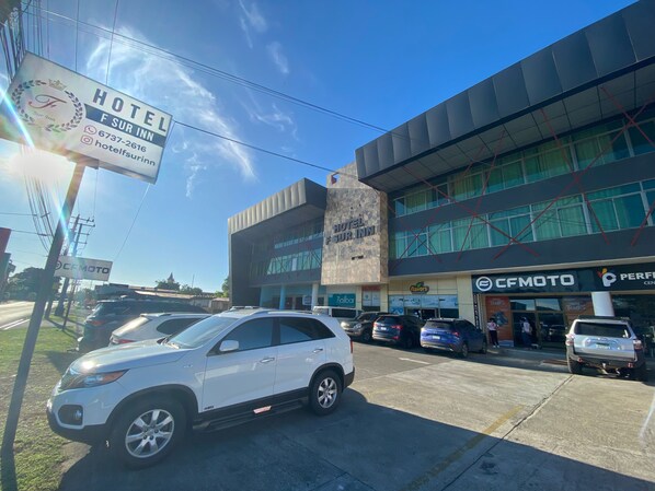 A hotel with a signboard, a parking lot with several cars, and a building with a CFMoto store. - Hotel F Sur Inn (David Sur)