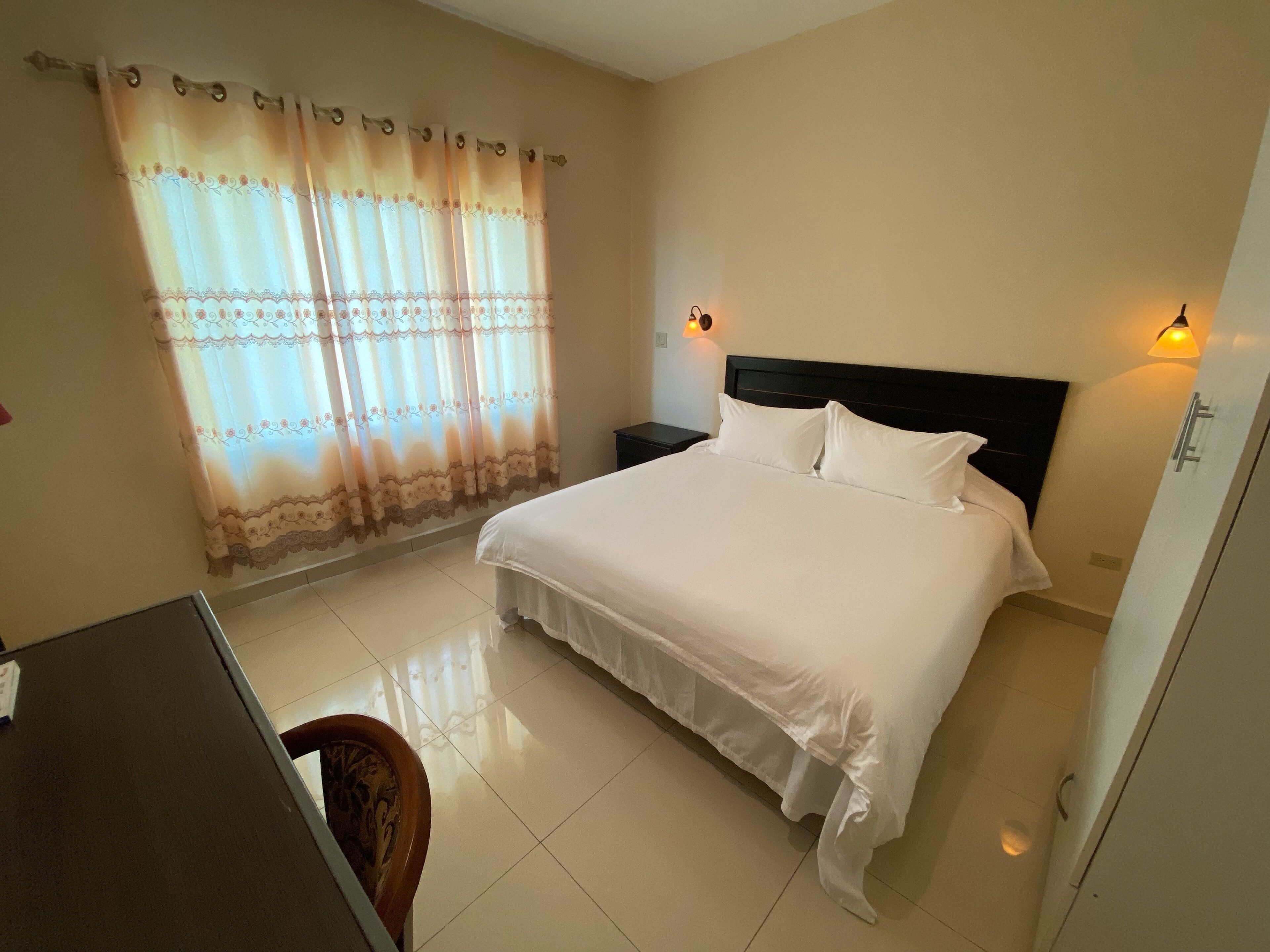 A hotel room with a large bed, a nightstand, a desk, and a chair.