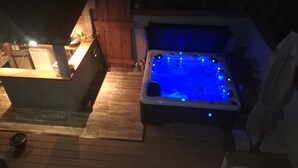 Un jacuzzi con iluminación azul, una terraza de madera y una pequeña cocina al aire libre.