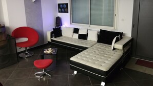 Una sala moderna con un sofá, un sillón rojo, una mesita y un ventilador de techo.