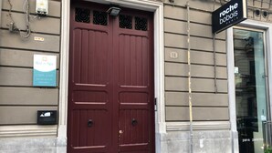 Unas grandes puertas dobles de color rojo oscuro con una celosía metálica, un cartel con la leyenda 'Bed in Spa' en la pared, y un letrero de 'Roche Bobois Paris' sobre la puerta.