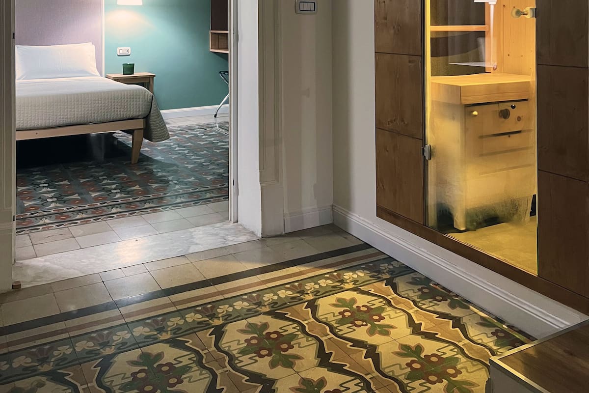 Una habitación de hotel con una cama, una mesita de noche, una alfombra estampada y un armario de madera con puerta de cristal.