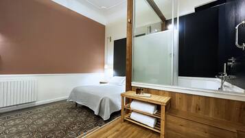 A hotel room with a large mirror, wooden floor, and a bed with a grey bedspread.