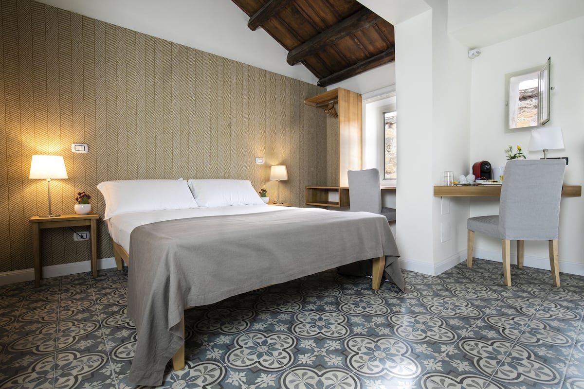 Un dormitorio ordenado con una cama grande, lámparas de noche, un escritorio con silla y baldosas de suelo estampadas.