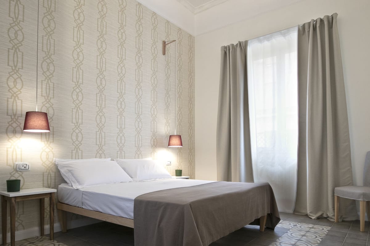 Un dormitorio ordenado con cama, mesitas de noche y una alfombra estampada.