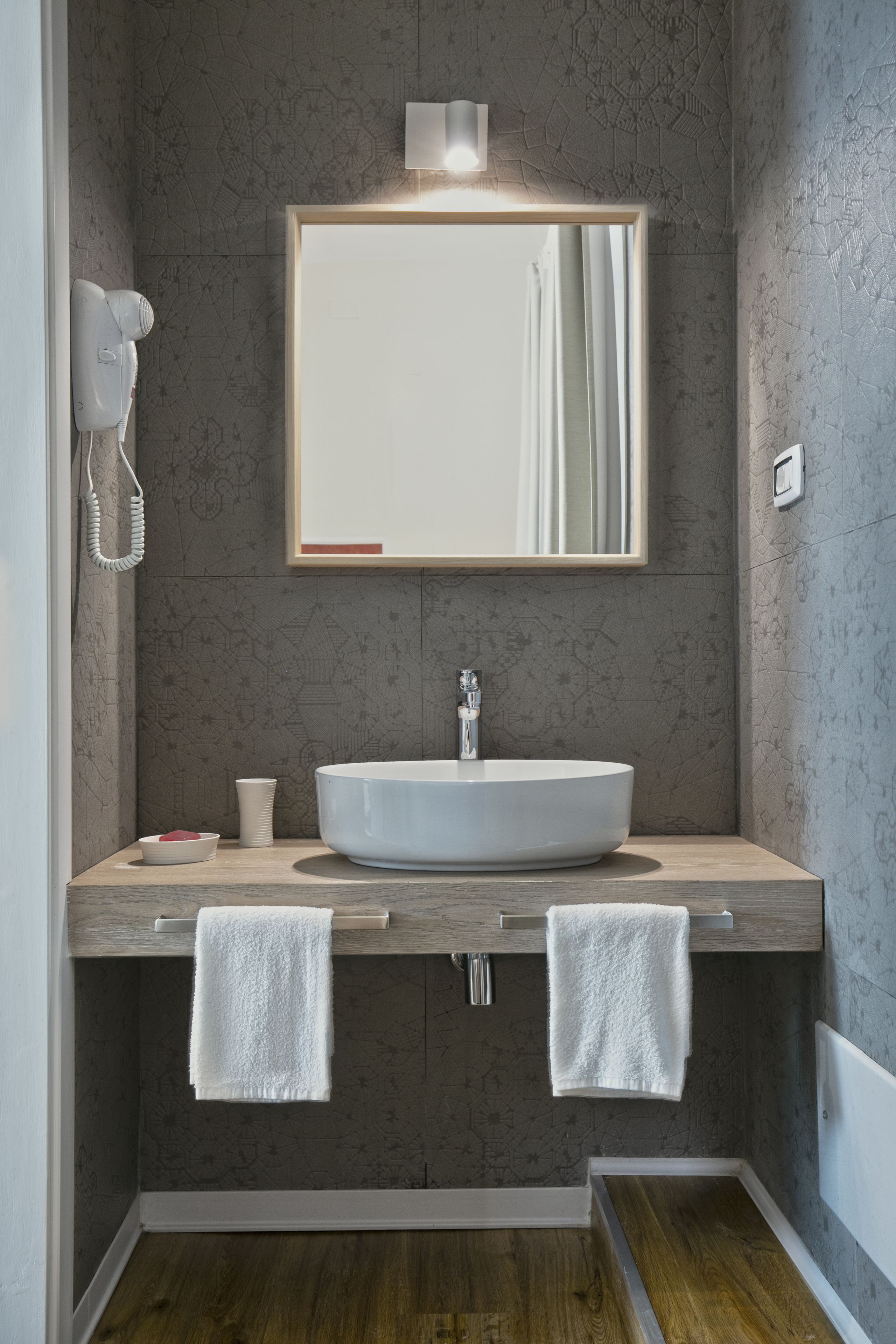 Ein modernes Badezimmer mit einem großen Spiegel, einem runden Waschbecken, zwei Handtüchern, einem Haartrockner und einer Tasse.