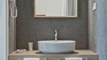 Ein modernes Badezimmer mit einem großen Spiegel, einem runden Waschbecken, zwei Handtüchern, einem Haartrockner und einer Tasse.