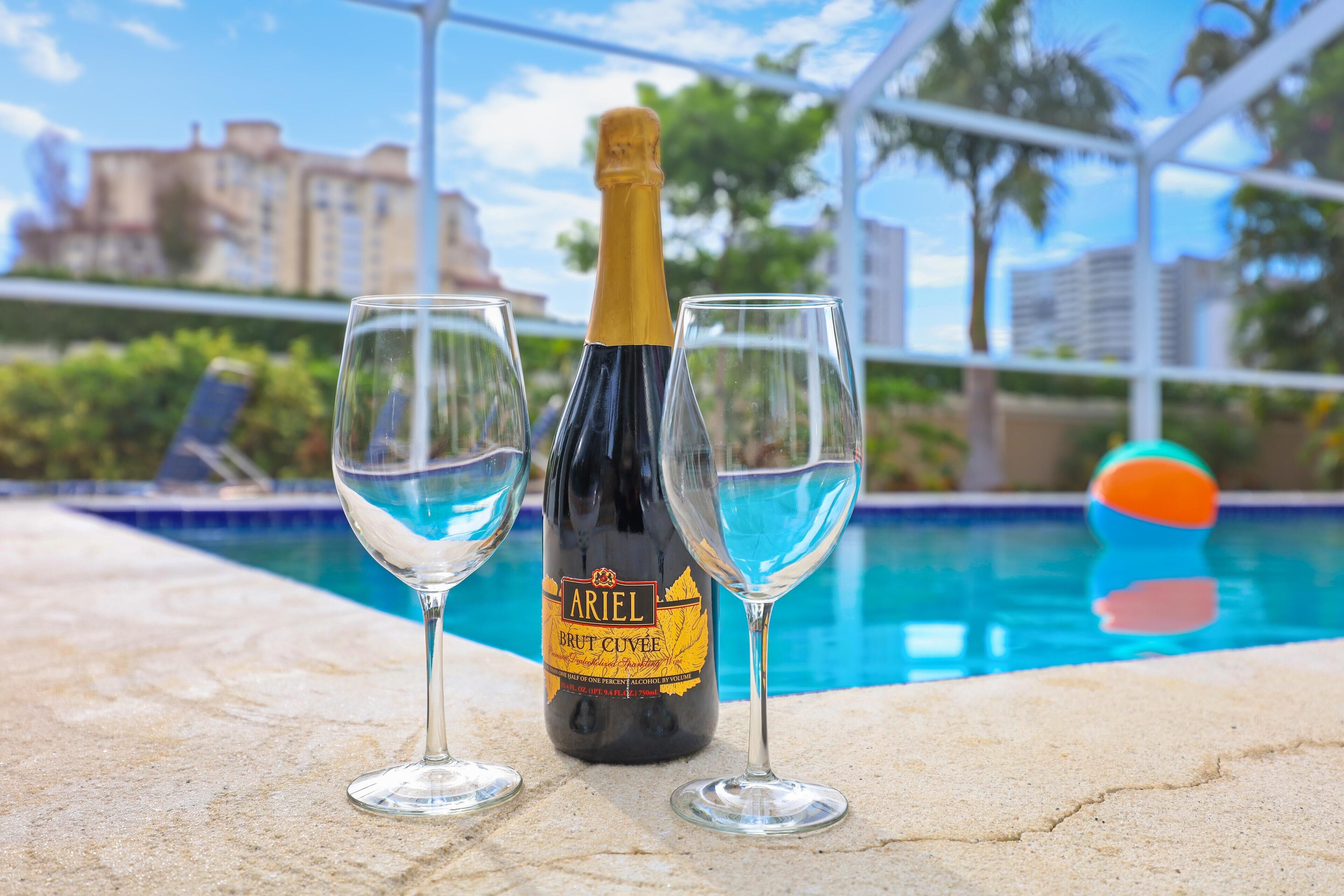 A bottle of Ariel Brut Cuvée champagne and two glasses on a poolside.