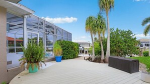 Un espace extérieur abrité, doté d’une terrasse en bois, de plantes en pot et d’une grande structure en verre.