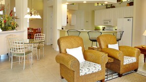 A spacious living room with wicker furniture, a dining area, and a kitchen with white cabinets. - 931 Hyacinth Court (Marco Island)