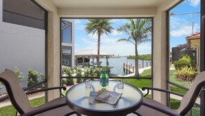 A balcony with a glass table, two chairs, a bottle of water, and a magazine. - Unique Waterfront Home With Pool, spa and Guesthouse (Marco Island)