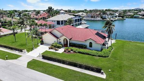 A residential property with a red-tiled roof, a well-maintained lawn, and a body of water in the background. - Unique Waterfront Home With Pool, spa and Guesthouse (Marco Island)