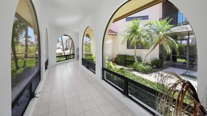 A corridor with large arched windows, tiled floor, and outdoor greenery visible through the windows. - Unique Waterfront Home With Pool, spa and Guesthouse (Marco Island)