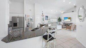 A modern kitchen with a granite countertop, stainless steel appliances, and a dining area with white furniture. - Luxuriously Furnished Waterfront Home With Pool/spa (Marco Island)