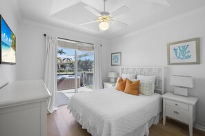A bedroom with a bed, nightstands, a ceiling fan, and a view of the outdoors. - Luxuriously Furnished Waterfront Home With Pool/spa (Marco Island)