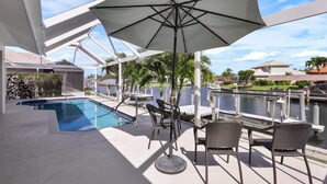A poolside area with a covered seating area, a pool, and a view of the waterway. - Luxuriously Furnished Waterfront Home With Pool/spa (Marco Island)