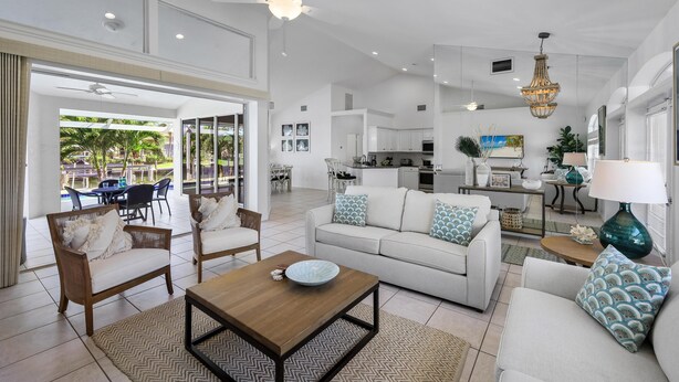 A spacious living room with a sofa, chairs, a coffee table, and a dining area with a chandelier. - Luxuriously Furnished Waterfront Home With Pool/spa (Marco Island)