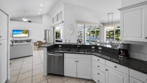 A modern kitchen with white cabinetry, a granite countertop, and a built-in dishwasher. - Luxuriously Furnished Waterfront Home With Pool/spa (Marco Island)