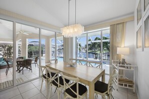 A spacious dining area with a large table and chairs, a chandelier, and a view of a swimming pool and greenery outside. - Luxuriously Furnished Waterfront Home With Pool/spa (Marco Island)