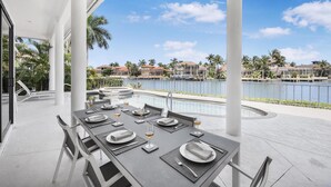 A dining area with tables set for four, overlooking a marina with boats and houses. - Waterfront Home on key lot With Pool, spa and Views (Marco Island)