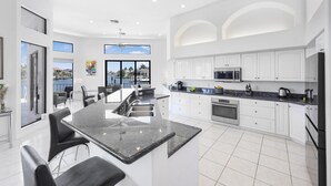 A modern kitchen with white cabinets, a large island, and a view of the outdoors. - Waterfront Home on key lot With Pool, spa and Views (Marco Island)