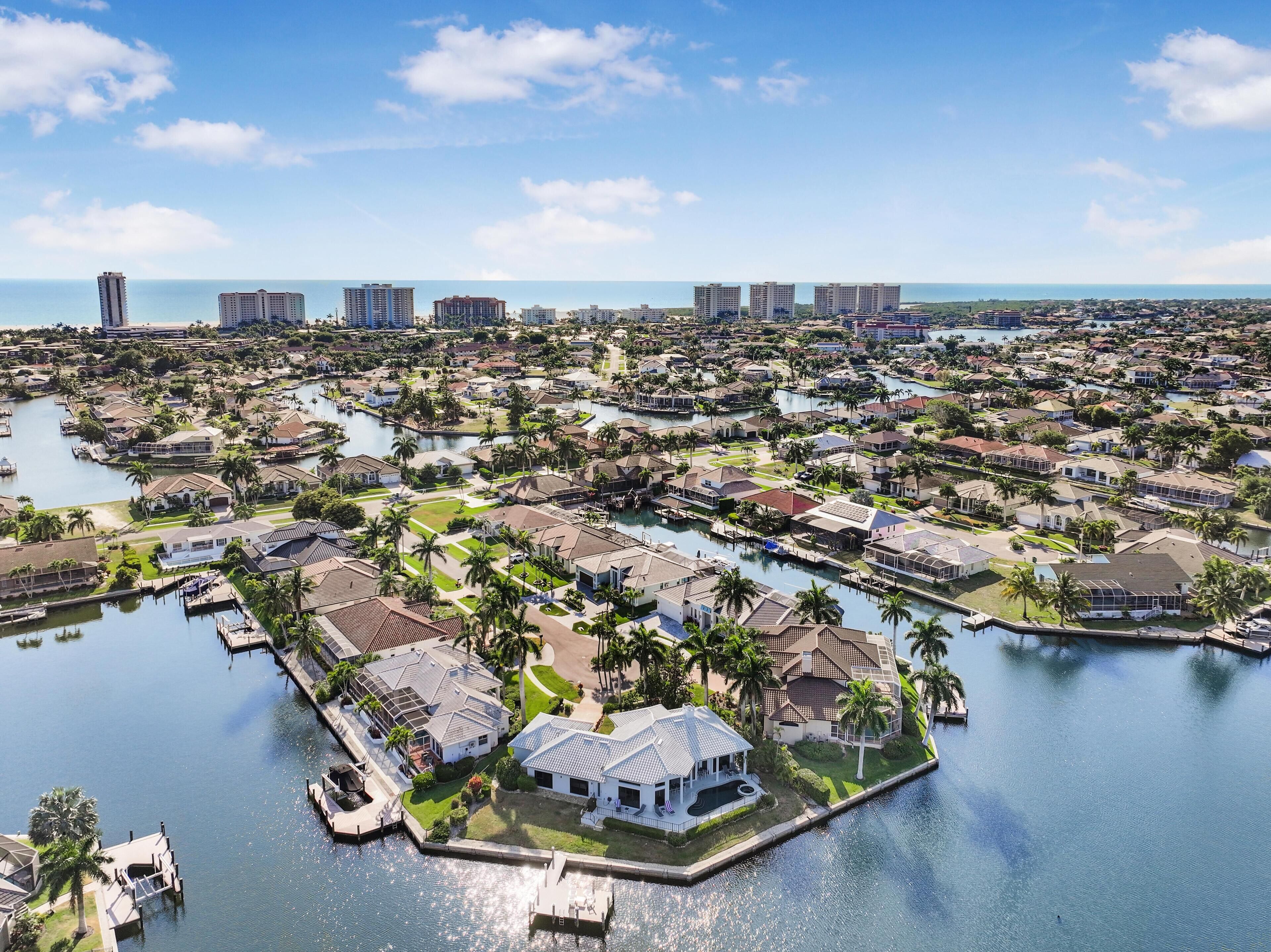 An aerial view of a coastal residential area with numerous houses, a marina, and a large body of water.