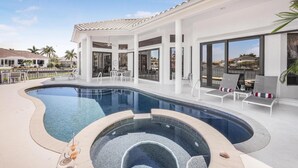 A modern pool area with a curved design, lounge chairs, and a clear view of the surrounding neighborhood. - Waterfront Home on key lot With Pool, spa and Views (Marco Island)