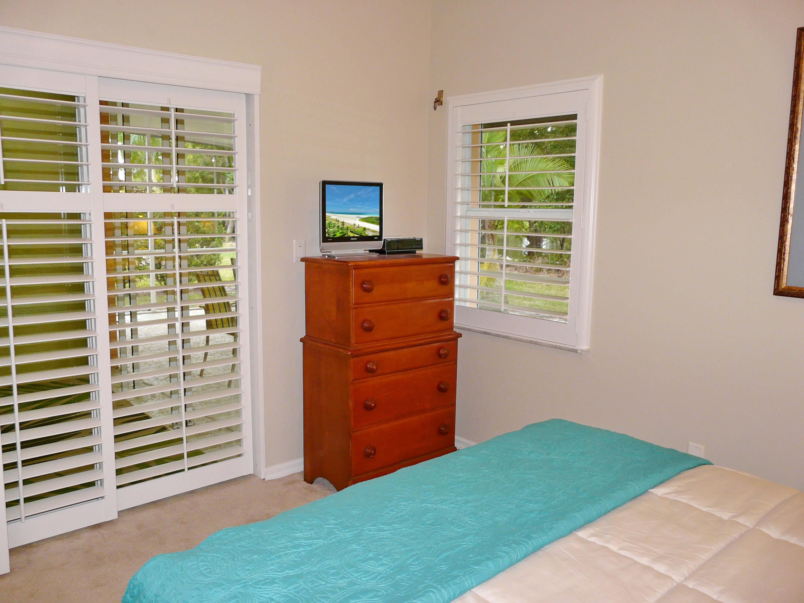 A bedroom with a bed, a dresser, and two windows with blinds.