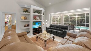 A living room with a sofa, a coffee table, a TV, and a bookshelf. - Peaceful Home With Pool and Steps to Beach/dining (Marco Island)