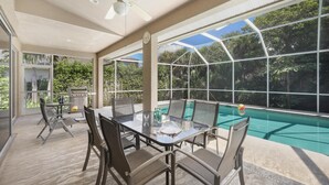 An outdoor patio with a glass table and chairs, a ceiling fan, and a view of a swimming pool. - Peaceful Home With Pool and Steps to Beach/dining (Marco Island)