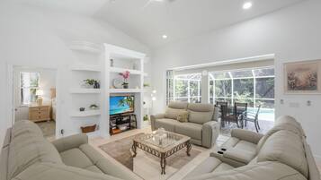 A spacious living room with a flat-screen TV, two sofas, a coffee table, and a dining area with a view of the outdoors.