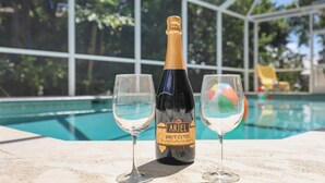 A bottle of Ariel Brut Cuvée champagne with two glasses on a table by a poolside. - Peaceful Home With Pool and Steps to Beach/dining (Marco Island)