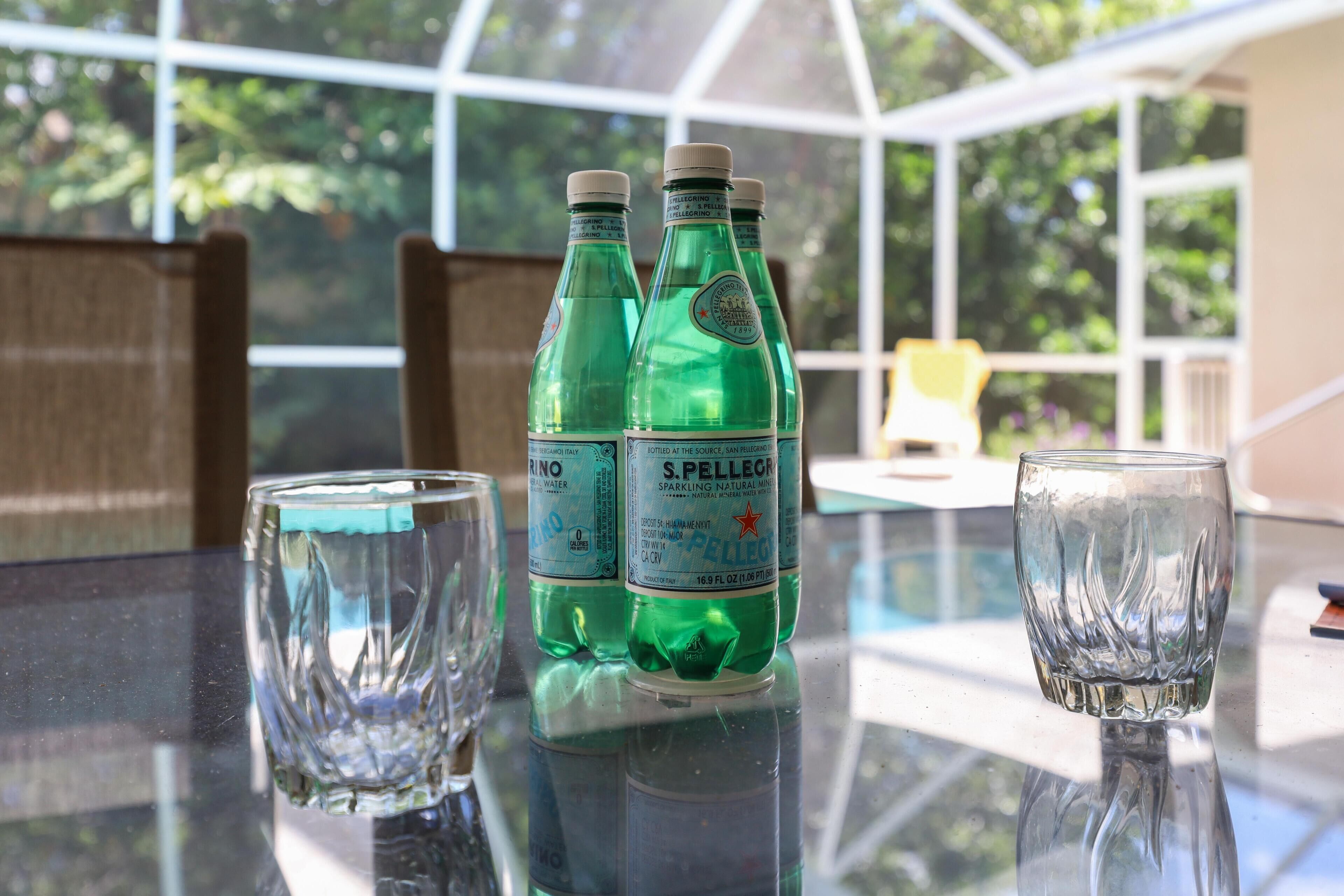 Three S. Pellegrino sparkling water bottles on a glass table with two empty glasses.