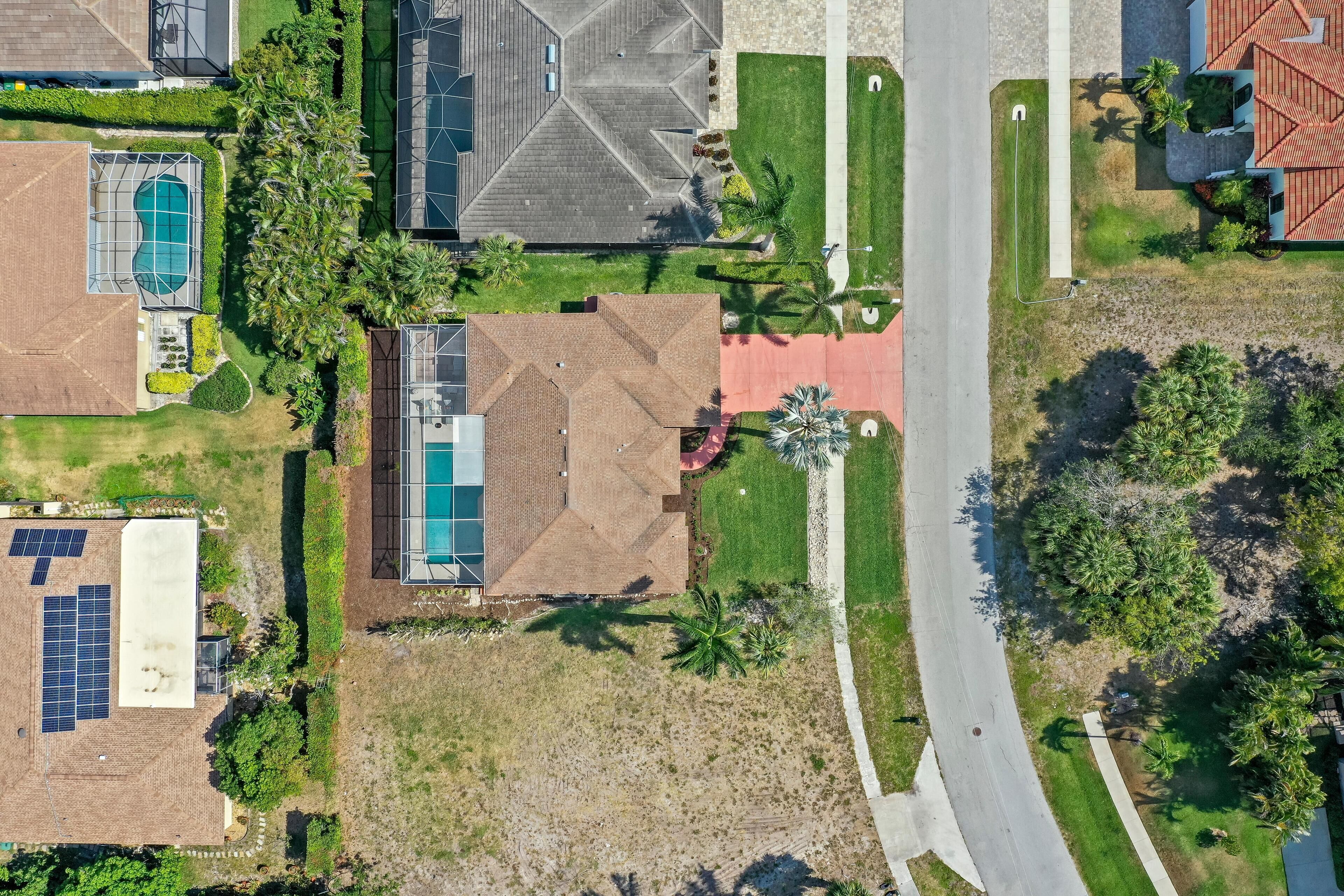 An aerial view of a residential area with a swimming pool, solar panels, and a road.