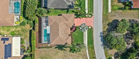 An aerial view of a residential area with a swimming pool, solar panels, and a road.