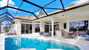 A pool area with a glass-enclosed patio, lounge chairs, and a barbecue setup.