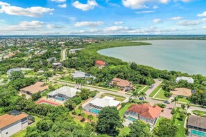 An aerial view of a residential area with houses, a large body of water, and a distant city skyline. - 550 Inlet Drive (Marco Island)