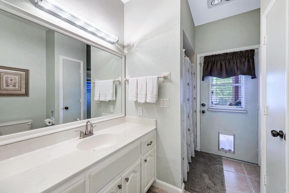 A bathroom with a large mirror, white vanity, and a shower with a window.