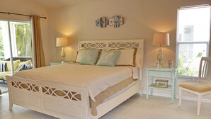 A bedroom with a large bed, two bedside tables with lamps, a chair, and a view of the outdoors. - 1292 Bayport Avenue (Marco Island)