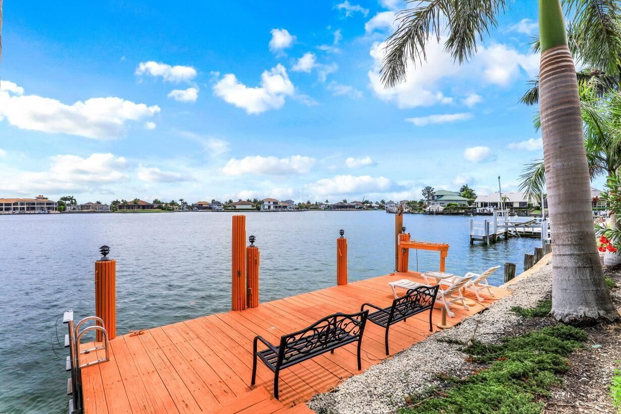 A wooden dock with benches and a palm tree, overlooking calm water with a clear sky.