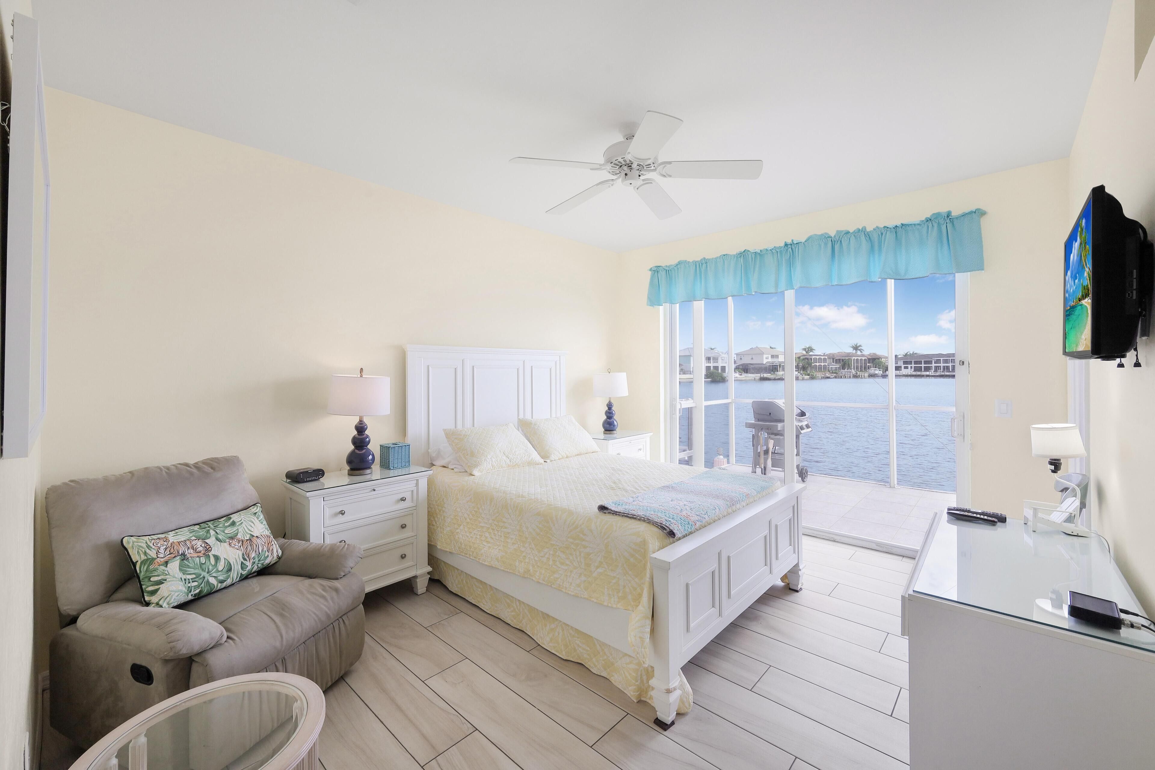 A bedroom with a bed, a nightstand, a chair, a desk, and a view of the water.