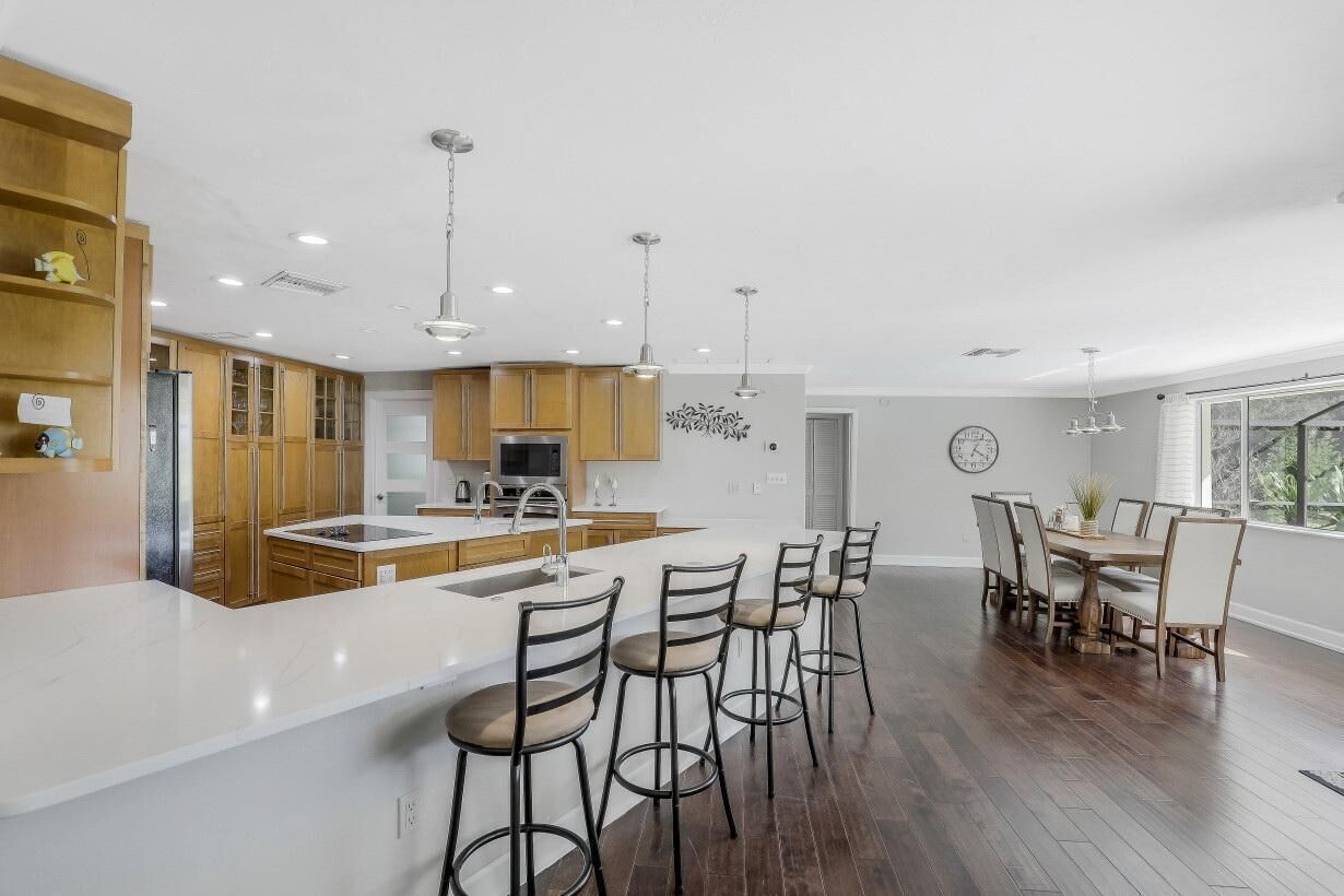 Una cocina moderna con armarios de madera, una isla central, taburetes de bar y un comedor con mesa y sillas.