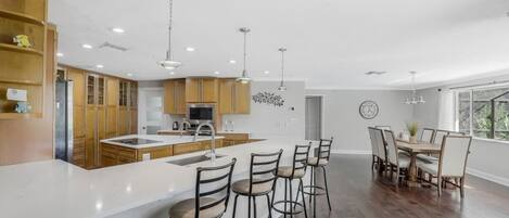 Una cocina moderna con armarios de madera, una isla central, taburetes de bar y un comedor con mesa y sillas.