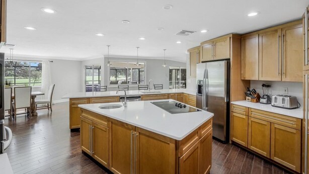 A modern kitchen with wooden cabinets, a large island with a sink, and stainless steel appliances. - 216 Shadowridge Court (Marco Island)