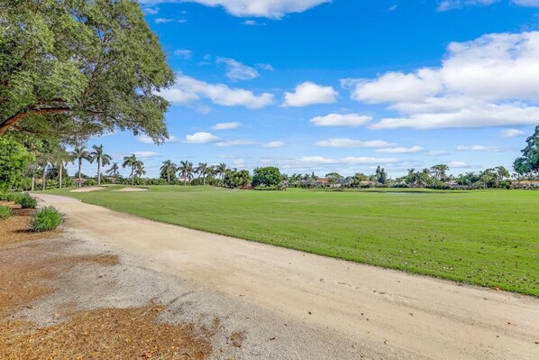 A golf course with a clear path, lush green grass, and palm trees in the background.